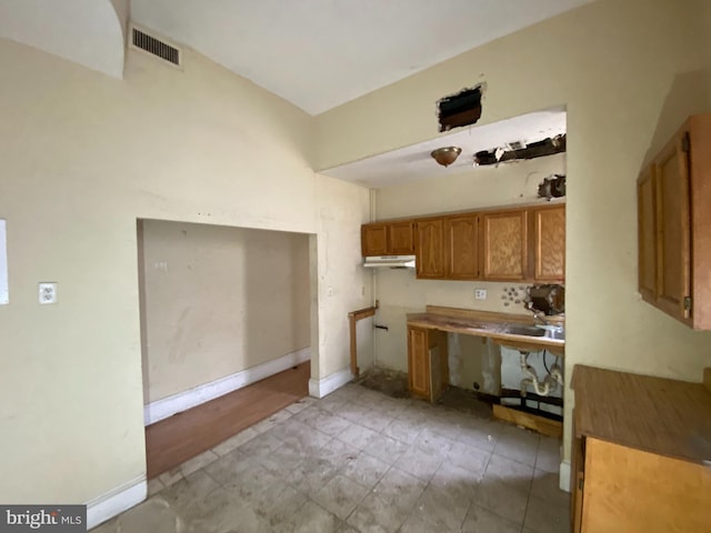 2110 N Charles St N, Baltimore, MD 21218 - kitchen with brown cabinets, under cabinet range hood, light tile patterned flooring, and light countertops