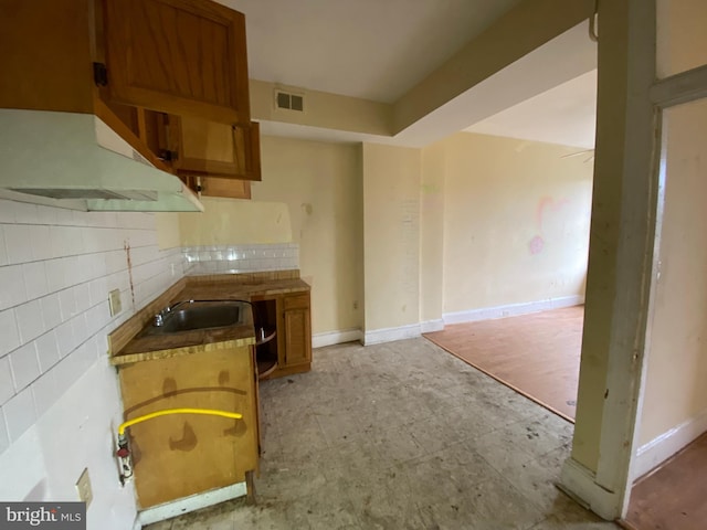 2110 N Charles St N, Baltimore, MD 21218 - kitchen with under cabinet range hood, backsplash, light floors, and brown cabinets