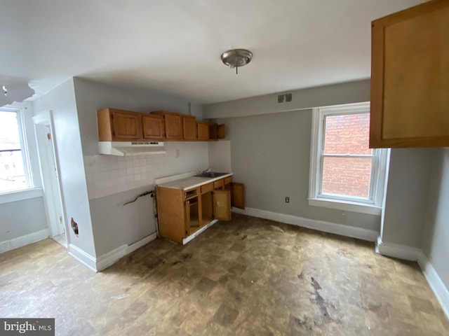 2110 N Charles St N, Baltimore, MD 21218 - kitchen with under cabinet range hood, brown cabinetry, tasteful backsplash, and light countertops