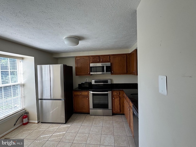 8902 Chesapeake Lighthouse Dr, North Beach, MD 20714 - kitchen featuring appliances with stainless steel finishes, dark countertops, light tile patterned flooring, brown cabinetry, and a textured ceiling