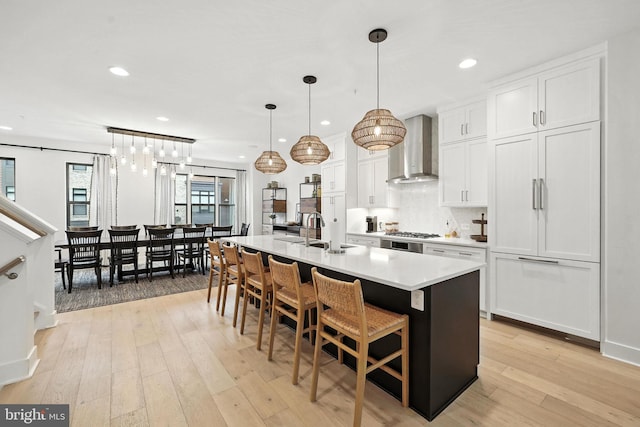 3536 Sutton Heights Cir, Fairfax, VA 22031 - kitchen with wall chimney exhaust hood, a center island with sink, white cabinetry, light countertops, and light wood-style floors