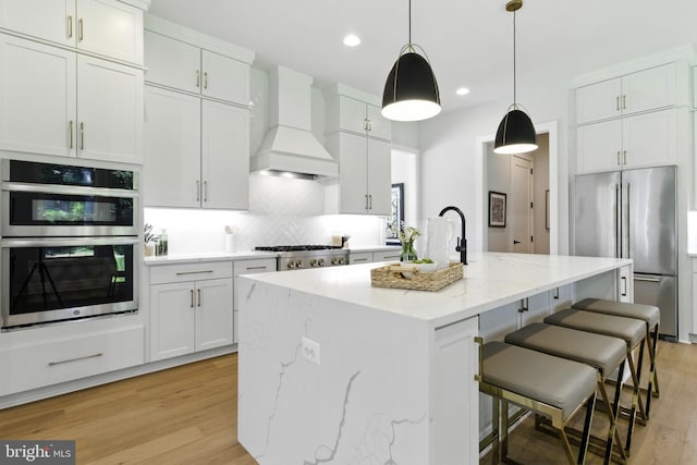 8202 Mockingbird Dr, Annandale, VA 22003 - kitchen with appliances with stainless steel finishes, premium range hood, light wood finished floors, an island with sink, and white cabinets