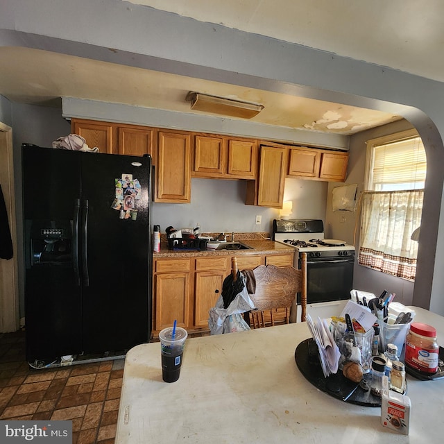 3648 Benson Ave, Baltimore, MD 21227 - kitchen featuring black fridge, gas range oven, arched walkways, brown cabinets, and light countertops