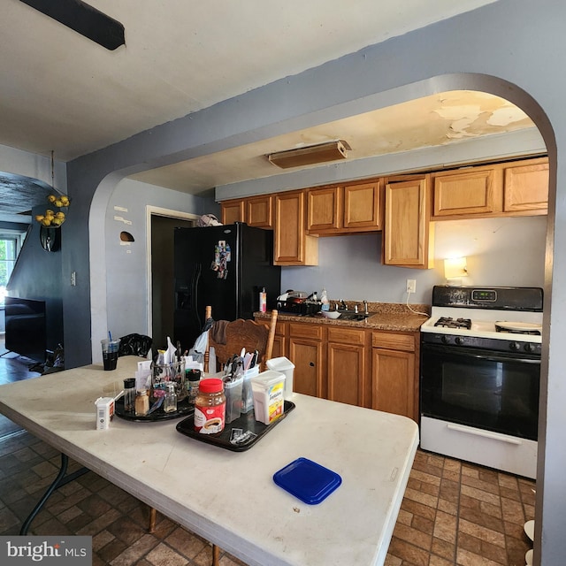 3648 Benson Ave, Baltimore, MD 21227 - kitchen featuring range with gas cooktop, arched walkways, black fridge, brick patterned flooring, and brown cabinetry