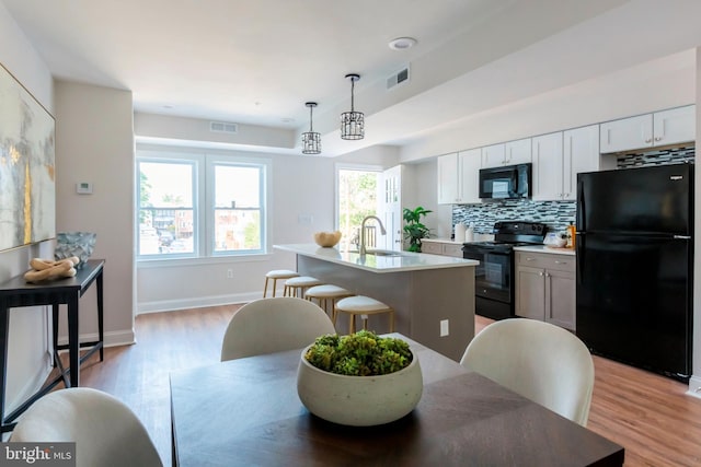 1616 C St NE, Washington, DC 20002 - kitchen featuring black appliances, light wood-type flooring, a kitchen island with sink, light countertops, and backsplash