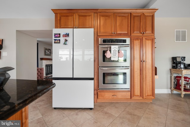 694 Ridge Rd, Telford, PA 18969 - kitchen with freestanding refrigerator, double oven, light tile patterned flooring, dark stone countertops, and brown cabinets