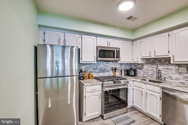 108 Wrangel Ct Unit 1, Princeton, NJ 08540 - kitchen featuring appliances with stainless steel finishes, tasteful backsplash, light stone counters, light wood-style flooring, and white cabinets