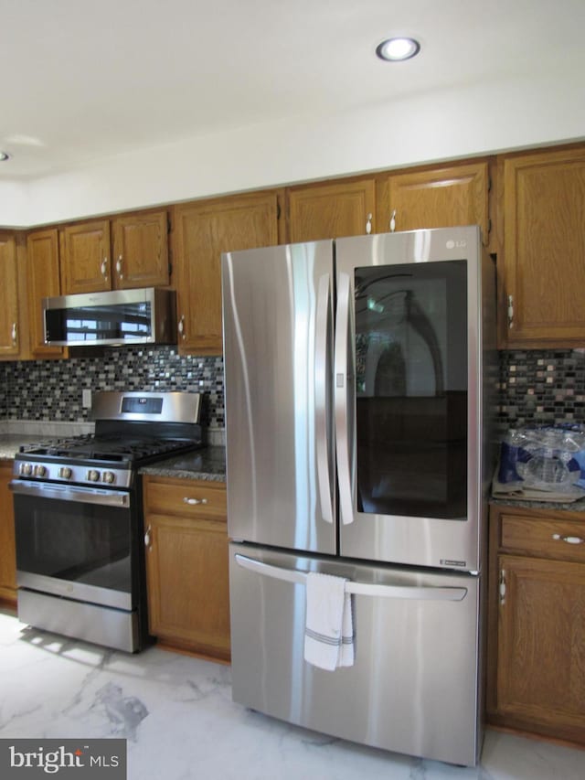 3590 Choptank Rd, Preston, MD 21655 - kitchen featuring appliances with stainless steel finishes, brown cabinets, backsplash, light marble finish flooring, and dark countertops