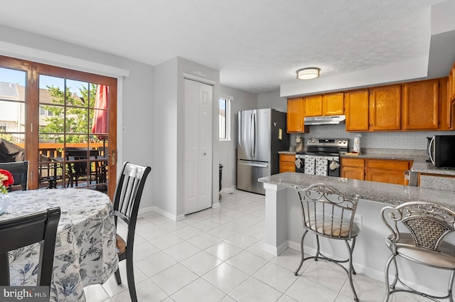 9258 Pirates Cv, Columbia, MD 21046 - kitchen featuring appliances with stainless steel finishes, brown cabinetry, under cabinet range hood, a peninsula, and decorative backsplash