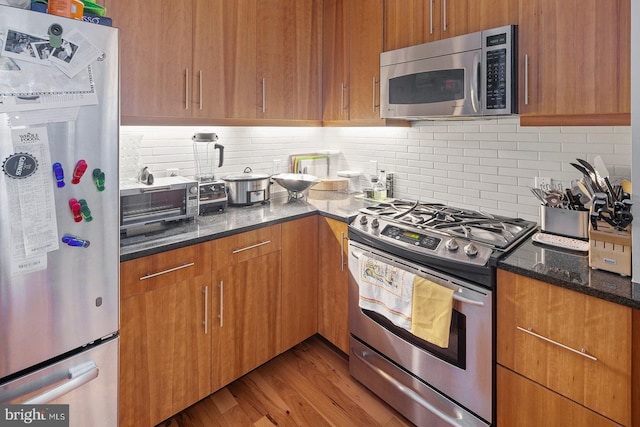 1425 Locust St Unit 5C, Philadelphia, PA 19102 - kitchen with appliances with stainless steel finishes, dark stone countertops, backsplash, wood finished floors, and brown cabinetry