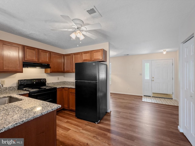 2635 Limestone Ct, Winchester, VA 22601 - kitchen featuring black appliances, under cabinet range hood, brown cabinetry, light stone counters, and a textured ceiling