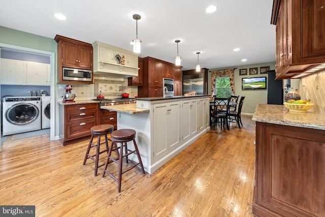 4105 Meadow Ln, Newtown Square, PA 19073 - kitchen featuring washing machine and clothes dryer, appliances with stainless steel finishes, light wood-type flooring, a kitchen island with sink, and a kitchen breakfast bar