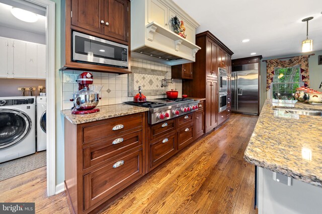 4105 Meadow Ln, Newtown Square, PA 19073 - kitchen featuring appliances with stainless steel finishes, washing machine and dryer, light wood-style floors, tasteful backsplash, and light stone counters