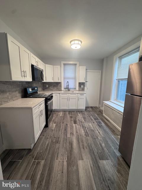 3302 N Palethorp St, Philadelphia, PA 19140 - kitchen featuring appliances with stainless steel finishes, dark wood finished floors, white cabinets, light countertops, and decorative backsplash