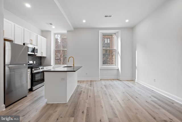 1805 Chestnut St, Philadelphia, PA 19103 - kitchen featuring appliances with stainless steel finishes, light wood finished floors, dark countertops, white cabinets, and tasteful backsplash
