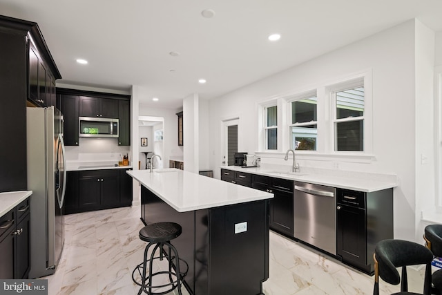 1227 Cross Rd, Annapolis, MD 21403 - kitchen featuring appliances with stainless steel finishes, a kitchen island with sink, light marble finish flooring, a kitchen bar, and dark cabinetry