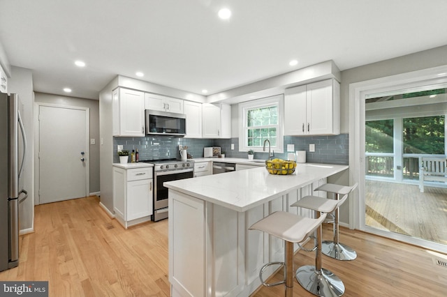 6 Ivywood Ct, Silver Spring, MD 20904 - kitchen with stainless steel appliances, a breakfast bar, tasteful backsplash, light wood-style flooring, and white cabinetry
