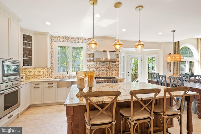 10915 Lamplighter Ln, Potomac, MD 20854 - kitchen featuring appliances with stainless steel finishes, wall chimney exhaust hood, a center island, backsplash, and light stone counters