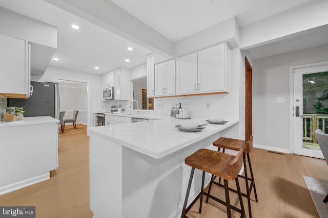 12779 Lost Creek Ct, Manassas, VA 20112 - kitchen featuring stainless steel appliances, a breakfast bar area, light wood-type flooring, tasteful backsplash, and white cabinetry