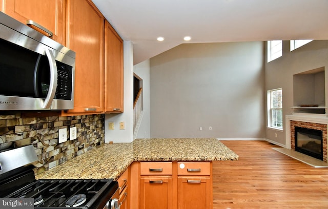 316 Wheatfield Cir, Hatfield, PA 19440 - kitchen with appliances with stainless steel finishes, a glass covered fireplace, decorative backsplash, light wood-style floors, and a peninsula