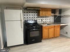 7128 Crestshire, Baltimore, MD 21222 - kitchen with black gas range, freestanding refrigerator, brown cabinets, light wood-style floors, and tasteful backsplash