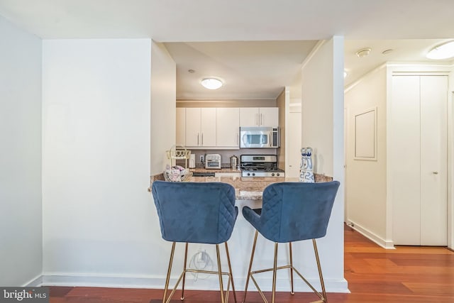 219 S 18th St Unit 1522, Philadelphia, PA 19103 - kitchen featuring appliances with stainless steel finishes, wood finished floors, a breakfast bar, a peninsula, and white cabinetry