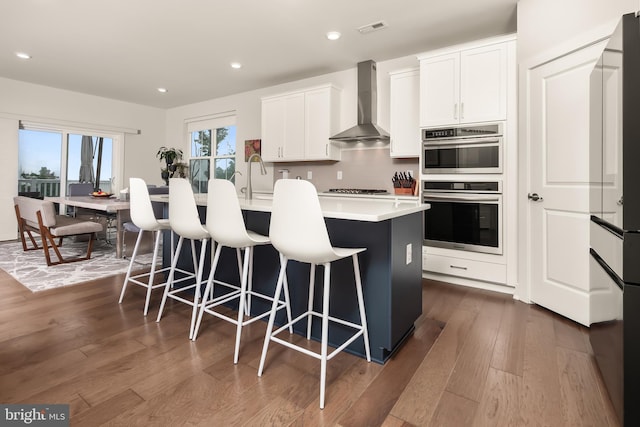 5635 Saucon Ridge Rd, Coopersburg, PA 18036 - kitchen featuring wall chimney range hood, double oven, an island with sink, dark wood finished floors, and recessed lighting