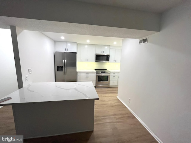 7720 Tremayne Pl Unit 107, Mclean, VA 22102 - kitchen featuring appliances with stainless steel finishes, light wood-type flooring, light stone counters, white cabinetry, and a peninsula