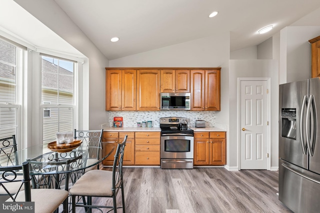 3709 Apple Cider Ct, Dumfries, VA 22025 - kitchen featuring stainless steel appliances, light wood-style floors, lofted ceiling, light countertops, and brown cabinetry