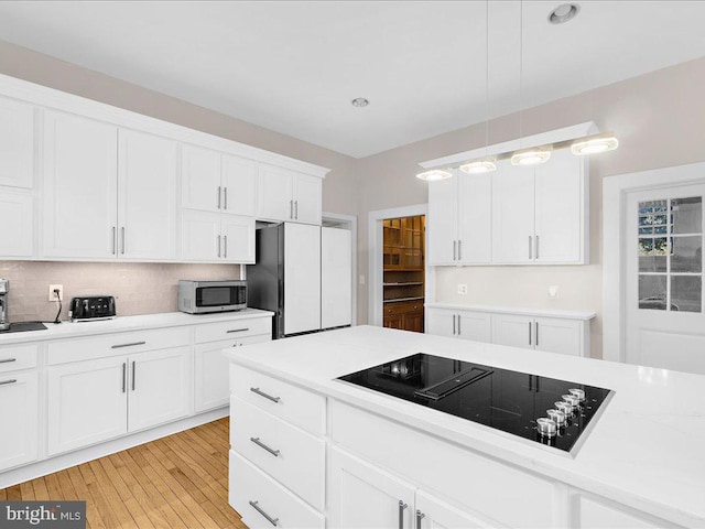 4332 N Charles St, Baltimore, MD 21218 - kitchen featuring black electric stovetop, stainless steel microwave, light countertops, white cabinets, and tasteful backsplash