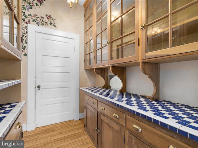 4332 N Charles St, Baltimore, MD 21218 - kitchen featuring tile countertops, light wood-type flooring, brown cabinets, and glass insert cabinets