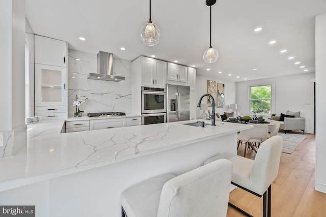 1539 K St SE, Washington, DC 20003 - kitchen featuring wall chimney exhaust hood, appliances with stainless steel finishes, light stone counters, a kitchen breakfast bar, and white cabinetry