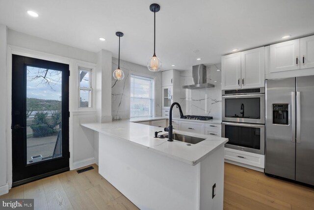 1539 K St SE, Washington, DC 20003 - kitchen featuring appliances with stainless steel finishes, wall chimney exhaust hood, white cabinets, backsplash, and light wood-type flooring