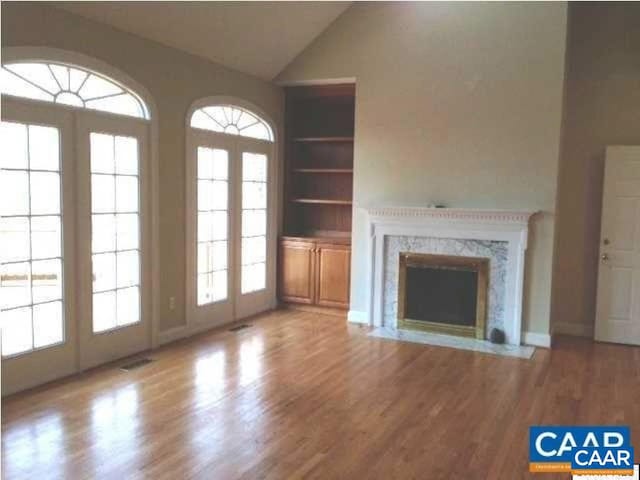 3190 Prestwick Pl, Keswick, VA 22947 - unfurnished living room featuring built in features, wood finished floors, vaulted ceiling, a premium fireplace, and french doors