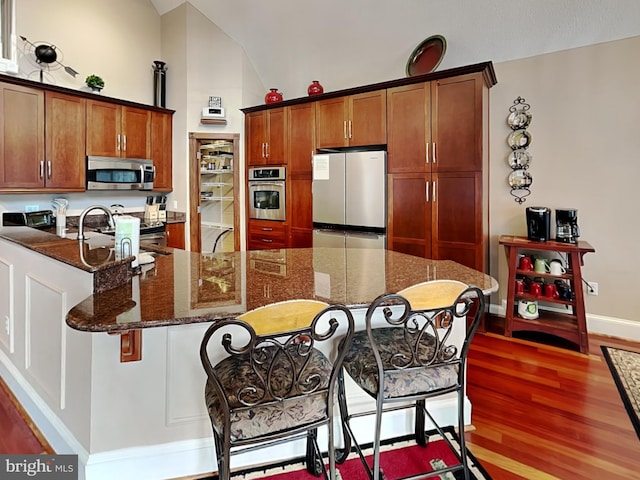 3067 Shingle Camp Rd, Mc Henry, MD 21541 - kitchen featuring appliances with stainless steel finishes, wood finished floors, a kitchen breakfast bar, dark stone countertops, and vaulted ceiling
