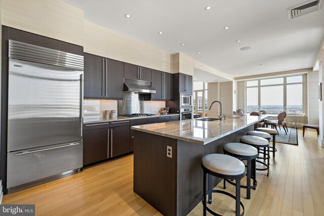 130 S 18th St Unit 3102, Philadelphia, PA 19103 - kitchen with built in appliances, under cabinet range hood, a breakfast bar, light wood-type flooring, and an island with sink