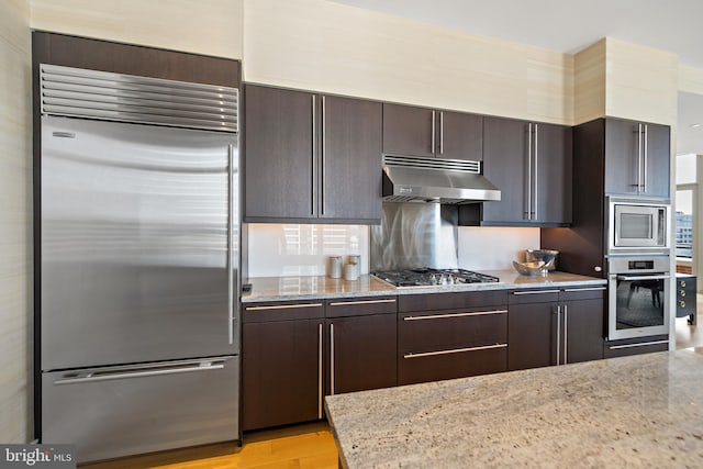 130 S 18th St Unit 3102, Philadelphia, PA 19103 - kitchen with built in appliances, under cabinet range hood, dark brown cabinetry, light wood finished floors, and light stone countertops