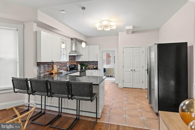 745 Gresham Pl NW, Washington, DC 20001 - kitchen featuring wall chimney exhaust hood, freestanding refrigerator, dark countertops, a peninsula, and white cabinets