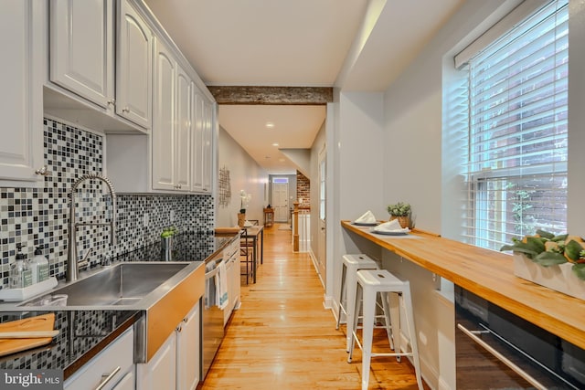 12 S Castle St, Baltimore, MD 21231 - kitchen featuring light wood-type flooring, backsplash, stainless steel dishwasher, and white cabinetry