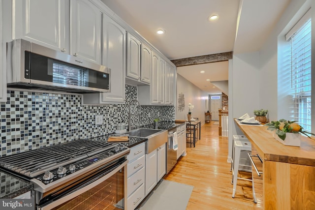 12 S Castle St, Baltimore, MD 21231 - kitchen with stainless steel appliances, light wood-style flooring, backsplash, butcher block counters, and beam ceiling