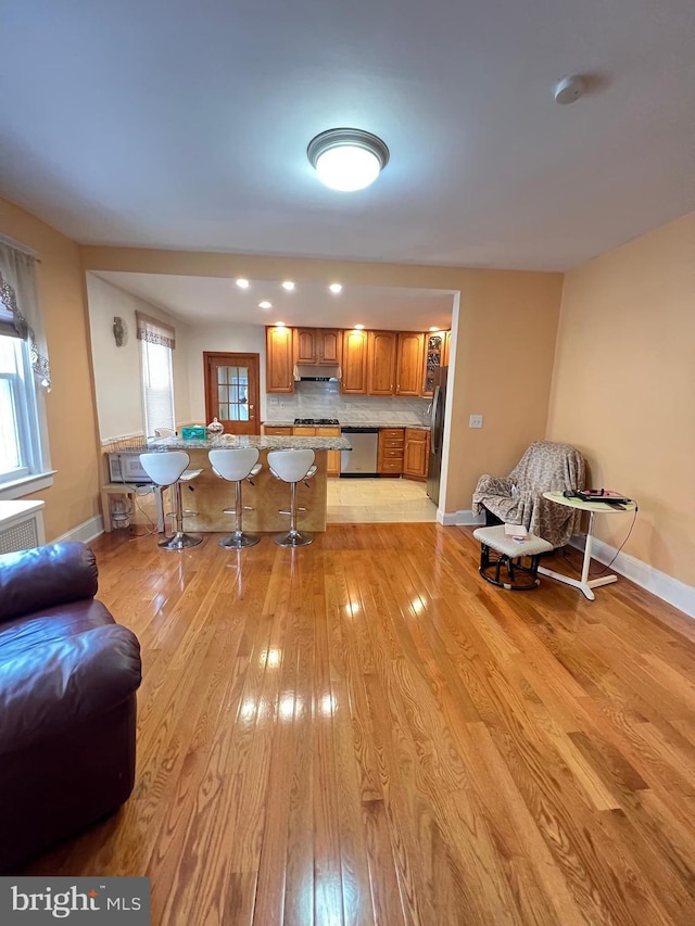 7033 Gillespie St, Philadelphia, PA 19135 - kitchen featuring appliances with stainless steel finishes, under cabinet range hood, brown cabinetry, a kitchen bar, and light wood-type flooring