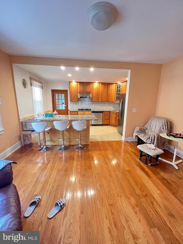 7033 Gillespie St, Philadelphia, PA 19135 - kitchen with appliances with stainless steel finishes, under cabinet range hood, brown cabinets, a kitchen breakfast bar, and light wood-type flooring