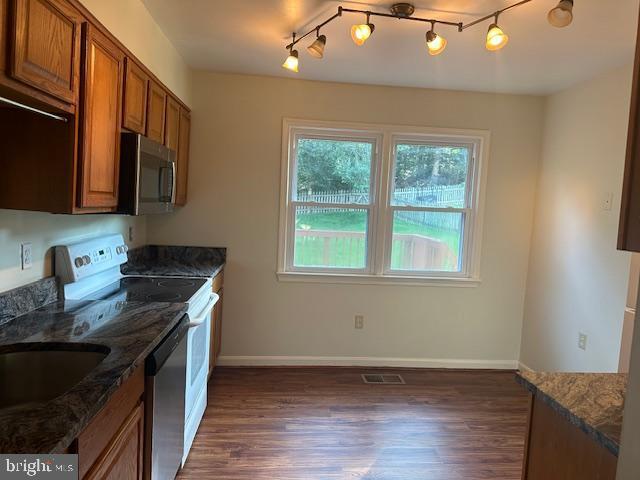 11876 Catoctin Dr, Woodbridge, VA 22192 - kitchen with stainless steel appliances, brown cabinetry, dark wood-style floors, dark stone countertops, and rail lighting