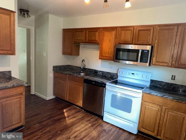 11876 Catoctin Dr, Woodbridge, VA 22192 - kitchen with appliances with stainless steel finishes, brown cabinetry, dark wood-type flooring, and dark stone counters