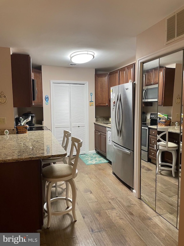 108 120th St Unit 6062, Ocean City, MD 21842 - kitchen featuring stainless steel appliances, light wood-style floors, a kitchen breakfast bar, light stone countertops, and dark brown cabinets
