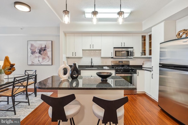 475 K St NW Unit 522, Washington, DC 20001 - kitchen featuring appliances with stainless steel finishes, a breakfast bar area, wood finished floors, white cabinets, and glass insert cabinets