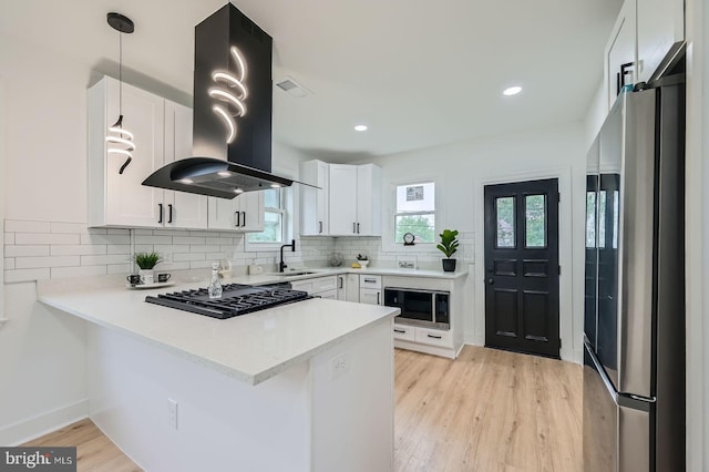 3814 Cedardale Rd, Baltimore, MD 21215 - kitchen with appliances with stainless steel finishes, island exhaust hood, a peninsula, backsplash, and light wood-type flooring