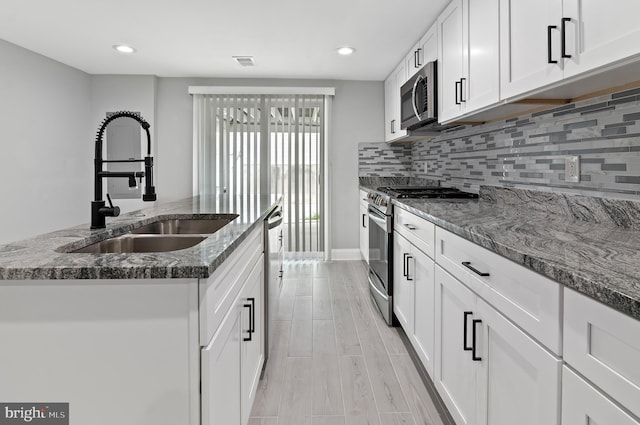 816 Carroll St, Baltimore, MD 21230 - kitchen with appliances with stainless steel finishes, an island with sink, dark stone counters, backsplash, and white cabinets