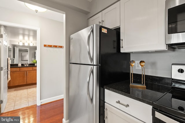 3401 38th St NW Unit 411, Washington, DC 20016 - kitchen featuring stainless steel appliances, white cabinets, light wood-style floors, and dark stone countertops