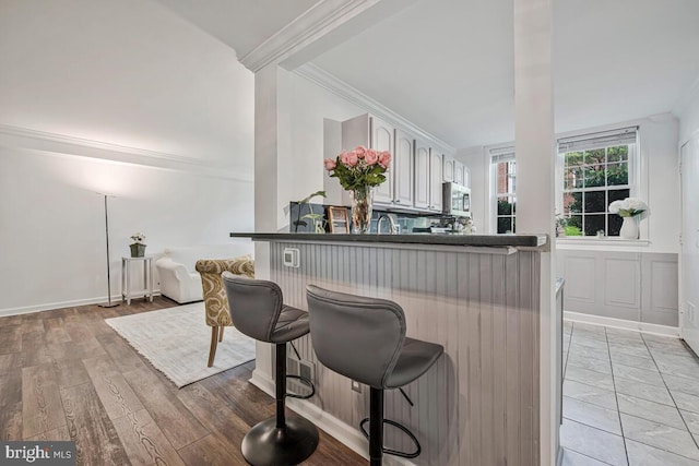 349 Homeland Southway Unit 1A, Baltimore, MD 21212 - kitchen featuring stainless steel microwave, crown molding, a breakfast bar, dark countertops, and light wood-style flooring